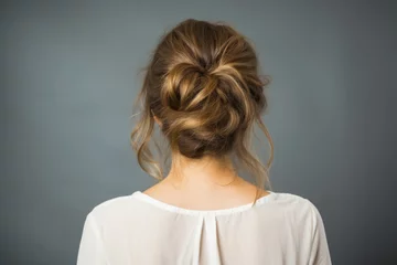 Tuinposter Back view of a girl head with hair in a messy bun hairstyle and simple top © Keitma