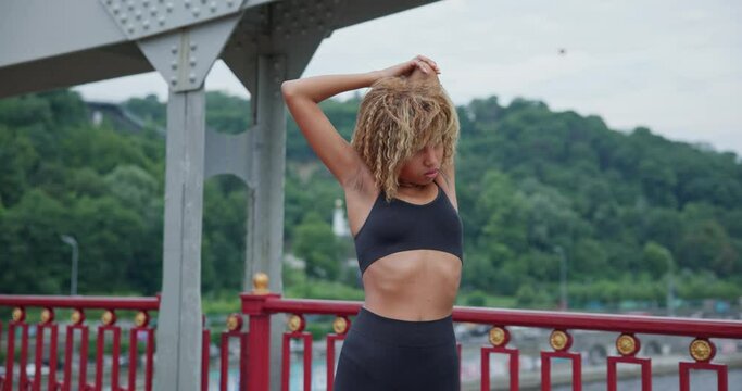 Fit young African American woman warming up and stretching before jogging on the bridge