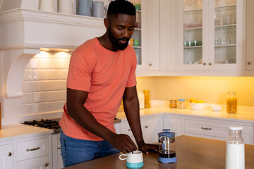 Happy african american man making coffee in white kitchen