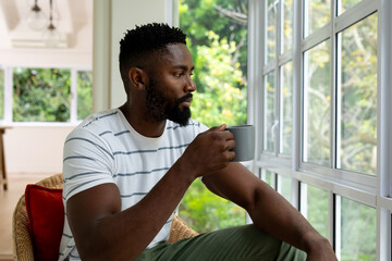 Thoughtful african american man drinking coffee and looking out window at home