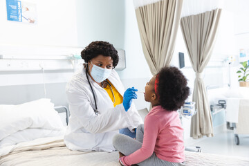 African american female doctor wearing face mask examining girl patient at hospital