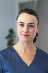Portrait of happy caucasian female doctor wearing blue scrubs in corridor at hospital