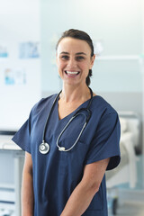 Portrait of happy caucasian female doctor wearing blue scrubs and stethoscope at hospital