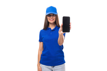 adorable european young brunette woman promoter in blue t-shirt and cap showing smartphone with mockup