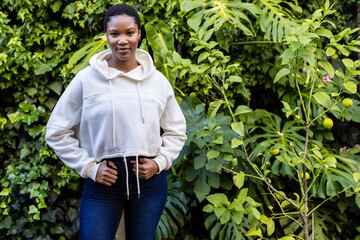 Naklejka na ściany i meble Portrait of happy african american woman in white hooded sweatshirt standing in garden, copy space