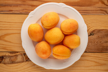 Naklejka na ściany i meble Several ripe juicy apricots in a white ceramic plate on a wooden table, macro, top view.