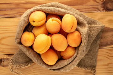 Several yellow sweet apricots in a jute bag on a wooden table, macro, top view.
