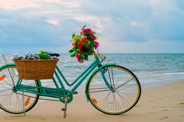 Papier Peint photo Vélo a vintage bicycle leaning against sea at beach in morning, Wicker basket with artificial flowers on the bike