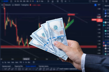 American dollar in man's hand and stock market screen, money chart background.