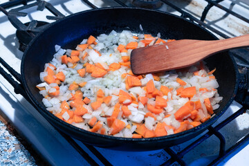 Carrots and onions are fried in a pan and mixed with a wooden spatula