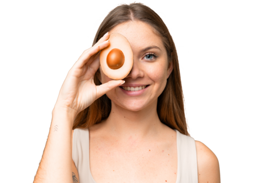 Young blonde woman over isolated chroma key background holding an avocado while smiling. Close up portrait