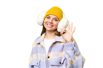 Young blonde woman wearing winter muffs over isolated chroma key background showing ok sign with fingers