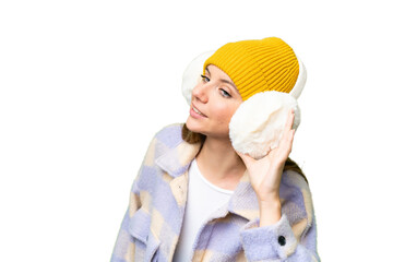 Young blonde woman wearing winter muffs over isolated chroma key background listening to something...