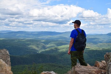 A man in a cap with a backpack stands on the top of a mountain and looks into the distance on a...