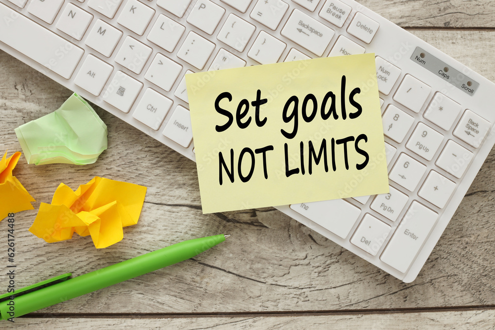 Poster set goals not limits text on yellow sticker on white keyboard. working table