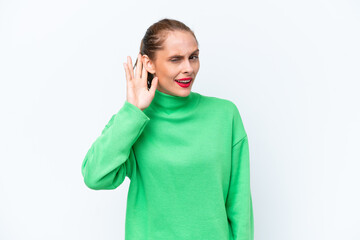 Young caucasian woman isolated on white background listening to something by putting hand on the ear