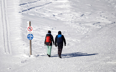 2 hikers on snow white hiking trail. Sign for path to the cross-country ski (Loipe) trail and pedestrians. Winter on the Feldberg in the Black Forest.