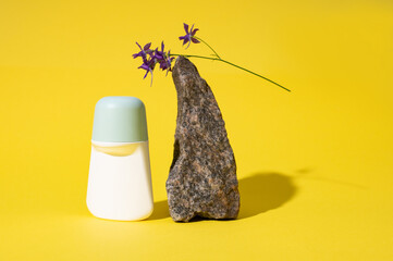 Still life with white mockup antiperspirant roller near a stone on a palm leaf, isolated on yellow studio background.