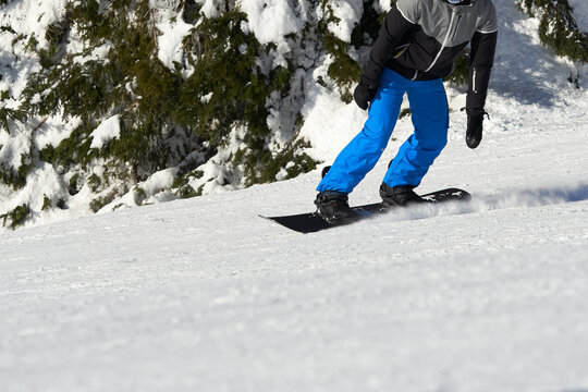 Male snowboarder on snow slope riding downhill. Detail of winter sportsman in Black Forest.