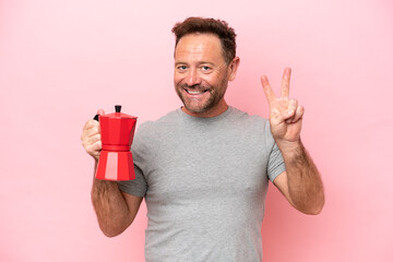 Middle age caucasian man holding coffee pot isolated on pink background smiling and showing victory...