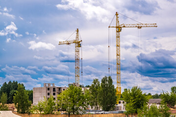two tower cranes working on construction with storm fluffy curly rolling clouds as background