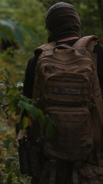 Soldiers with special equipment and backpacks trudge through the forest, navigating through dense vegetation and underbrush.