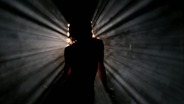 alluring woman dancing sensual dance in darkness, silhouette of sexy body against bright light