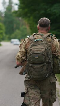 The military operative, equipped with a weapon and a backpack, is moving on the road.