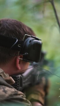 image of a military soldier positioned in a forest, gripping a firearm with their hands and peering intently through the scope.