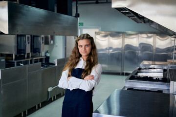 Single young girl in chef uniform portrait standing in real kitchen for education kitchen class concept.