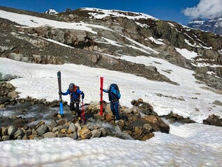 Ski tourers have to jump over a stream. Susten Pass above Meiringen in the canton of Bern. Ski mountaineering. High quality photo