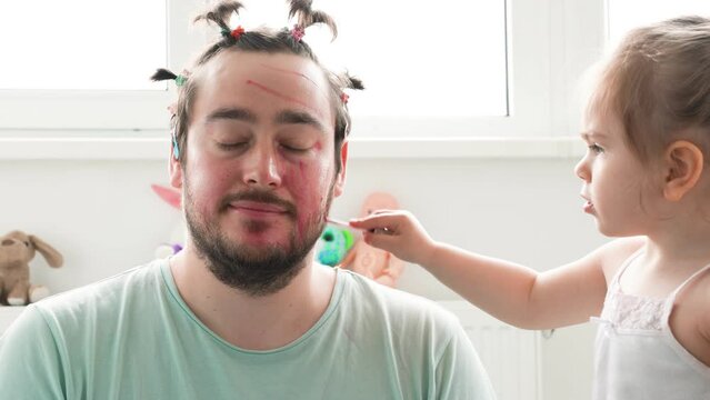A bearded dad and his daughter sharing a fun and playful moment while putting on makeup, with funny faces and expressions. Dad's First Time Putting Makeup on His Daughter Goes Terribly Wrong