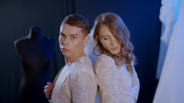 portrait of two gays in love, standing back to back in dark studio, wedding of lgbt people