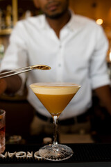 vertical photo of a bartender putting dried orange on top of the cocktail