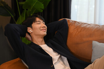 Obraz premium Pleasant millennial asian man lying on comfortable couch enjoy stress free peaceful mood at home