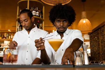 focused latin bartender with curly hair making a cocktail with his colleague next to him