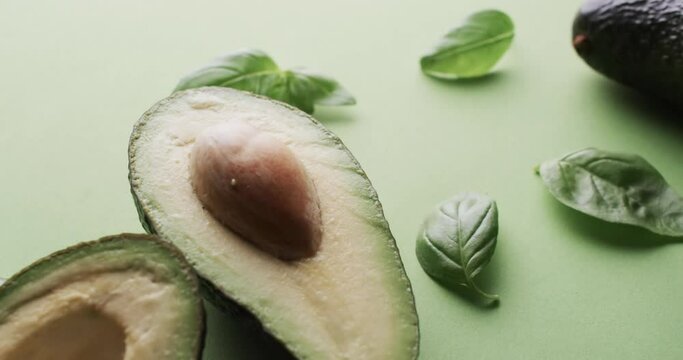 Video of sliced avocado and basil leaves with copy space over green background