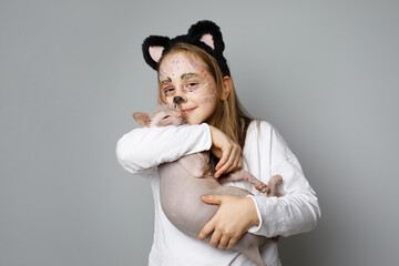 Happy lovely child girl with painted face embracing her cat, studio portrait