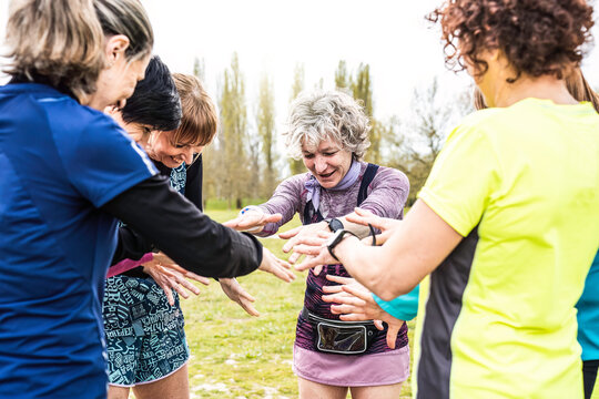 Happy multigenerational women stacking hands together before sport workout outdoor - Female friends having fun together outdoor at city park - Bright filter with focus on grey hair woman