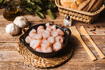 Raw prawns on a plate on a rustic table, with the ingredients to prepare them with garlic, close-up.