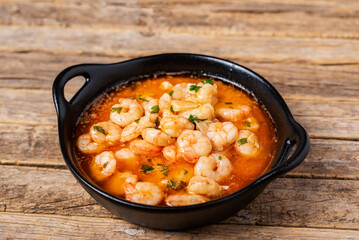 Black casserole dish with garlic prawns, or Pil-pil, on a rustic wooden table, close-up.