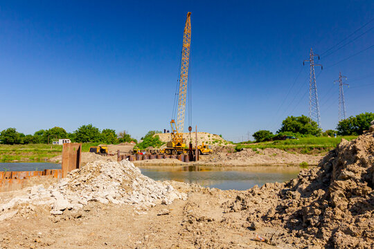 Bridge foundation made of metal piles on river coast, in background is old hoist with pneumatic hammer. Building site area