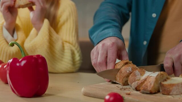 Unrecognizable man father cut bread little daughter eat breakfast at domestic home kitchen dinner happy family dad with child girl kid eating crispy tasty baguette food delivery close up at table