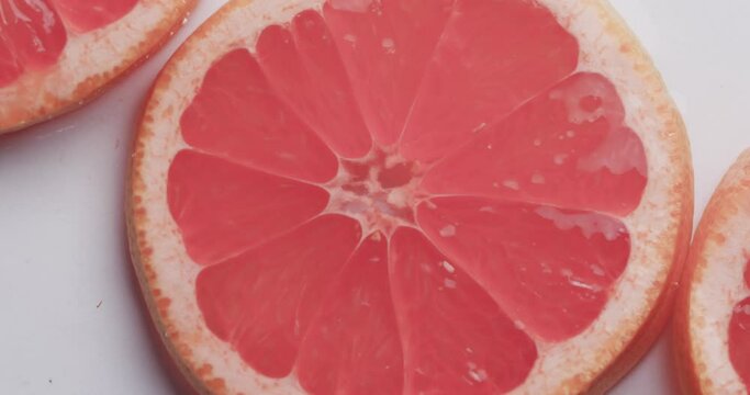Video of water drops falling onto slices of red grapefruit with copy space on white background