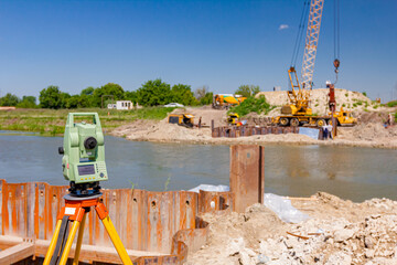 Total station on building site, in background is metal piles and hoist with pneumatic hammer
