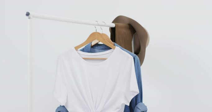 Video of white and denim t shirt on hangers, hat and copy space on white background