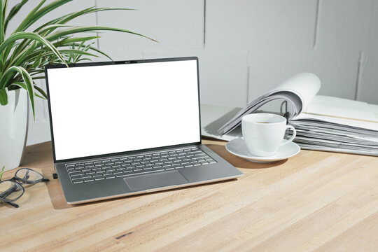 Mock up on an open laptop with a blank white screen, coffee cup and ring binder on a wooden office desk against a white painted wall, business concept, copy space