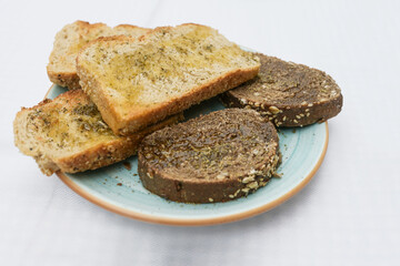 White and dark toasted bread with olive oil, herbs and garlic salt on a turquoise plate, copy space, selected focus