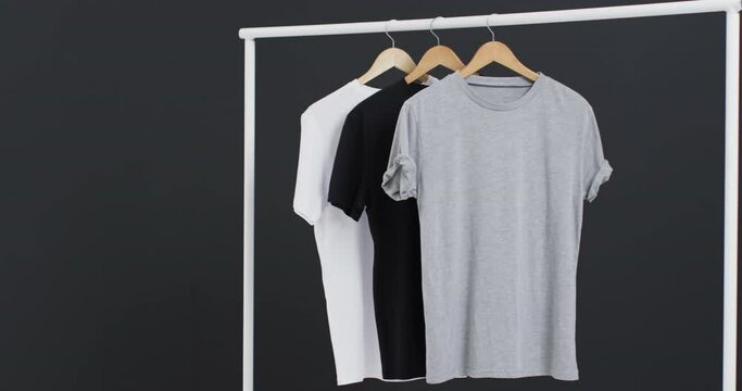 Video of three white, black and grey t shirts on hangers and copy space on black background