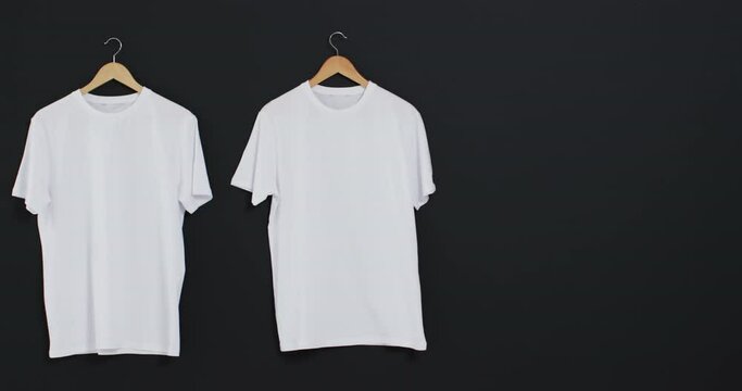 Video of two white t shirts on hangers and copy space on black background